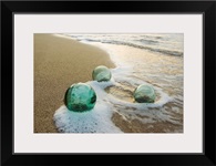 Three Glass Fishing Floats Roll On The Sandy Shoreline With Ripples Of Water And Seafoam