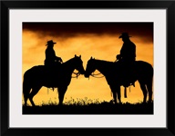 Cowboy and cowgirl on horseback in silhouette at sunset