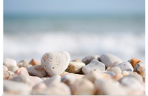 Directed focus on a heart shaped stone on a pebble beach in the foreground.