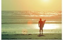 Surfer stands by shore as sun goes down.