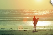 Surfer stands by shore as sun goes down.