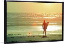 Surfer stands by shore as sun goes down.