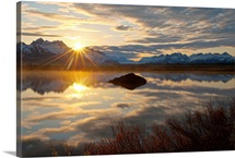 Sun rises over the Chugach Mountains with a pond and beaver lodge in the foreground