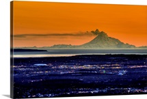 The city of Anchorage Alaska at sunset with Mount Redoubt erupting in the background