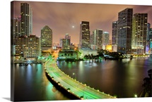 Bridge leads across waterway to downtown Miami sklyine at night.