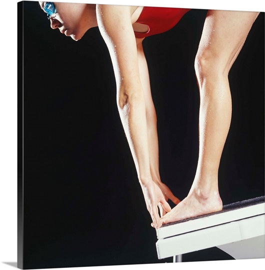 Female swimmer preparing to dive off starting block, close up, studio