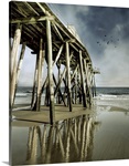 Fishing shack pier with reflection in sea and flock of birds in sky.