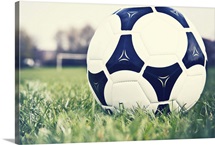 Football on football pitch with goal in distance.