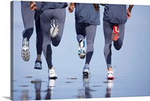Four men jogging on beach, low section, rear view