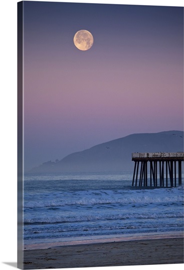 Full moon sets over  Pismo Beach at sunrise on winter morning.