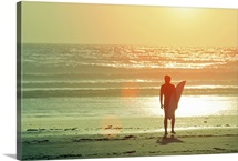 Surfer stands by shore as sun goes down.