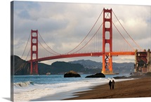 A couple strolling on Baker Beach near the Golden Gate Bridge at dawn