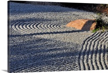 An embedded rock catches the afternoon sun in a raked rock garden