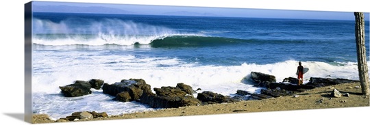 Surfer standing on the beach and looking at surf, Isla Natividad, Baja California, Mexico