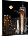 A nearly full Moon sets as Space Shuttle Discovery sits atop the launch pad