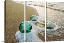 Three Glass Fishing Floats Roll On The Sandy Shoreline With Ripples Of Water And Seafoam