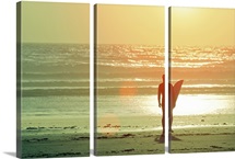 Surfer stands by shore as sun goes down.
