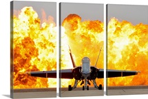 An F/A 18 Hornet sits on the flight line as a wall of fire detonates behind it