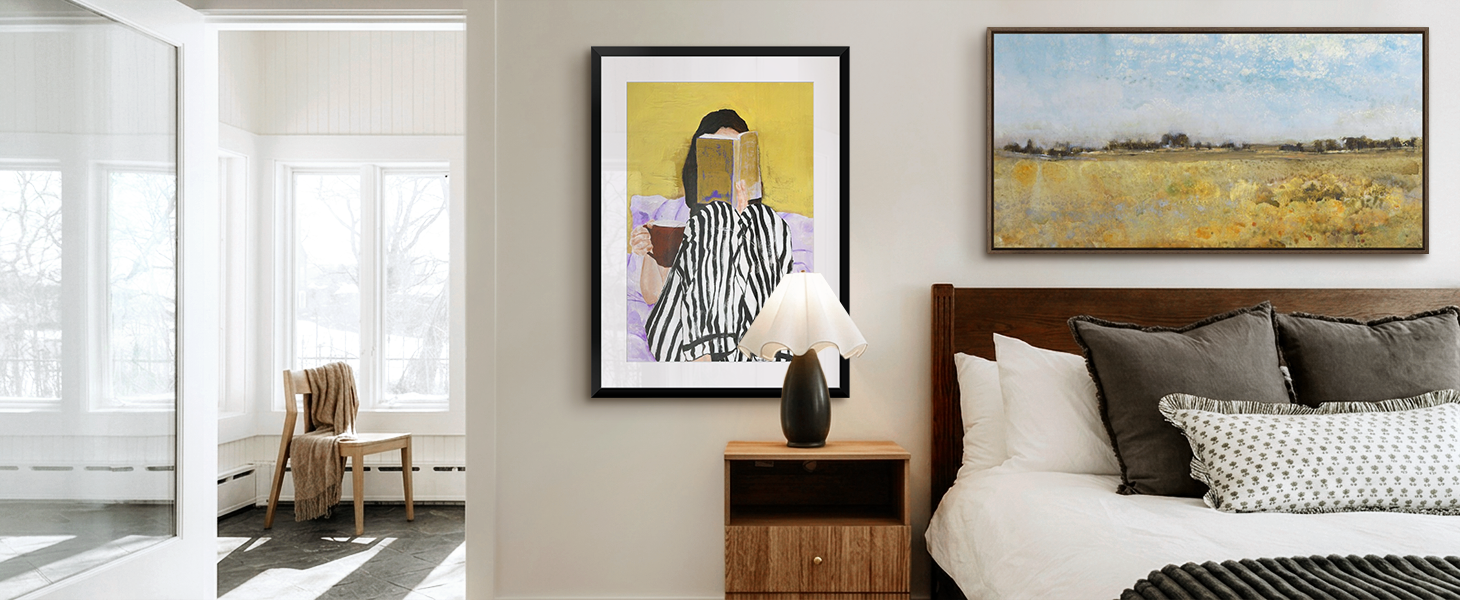 Framed print of a painting of a woman reading in bed and a framed canvas art print of a landscape hanging in a bedroom