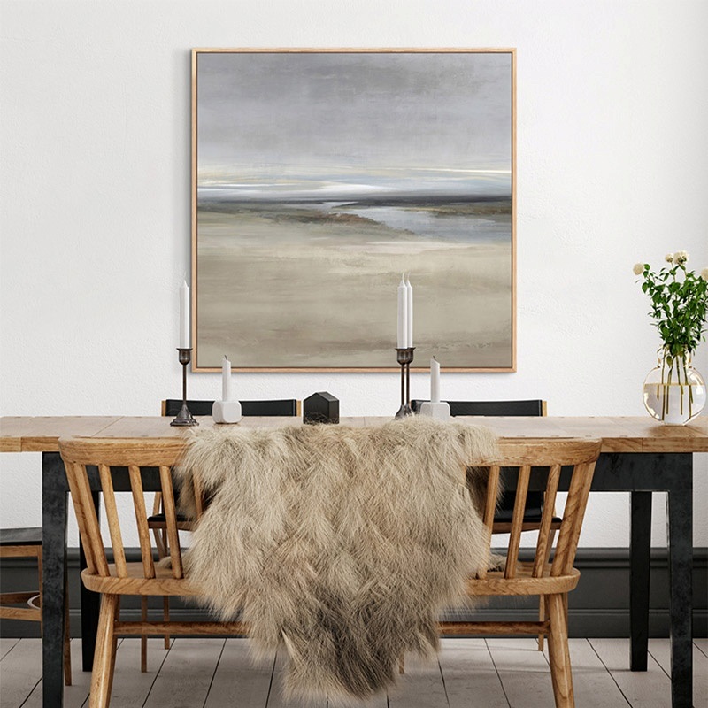 framed canvas of a neutral landscape hanging above a wooden dining room table