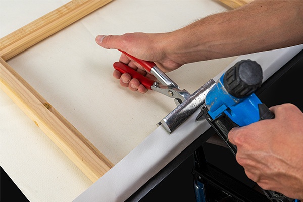 a person using tools to stretch and staple canvas over stretcher bars, as seen from the back side of