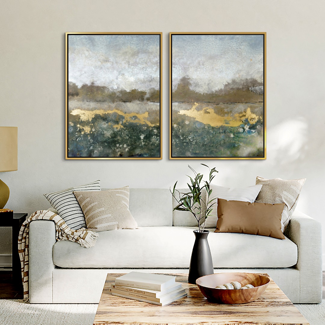 two landscapes canvas prints with gold accents in gold floating frames over a living room couch