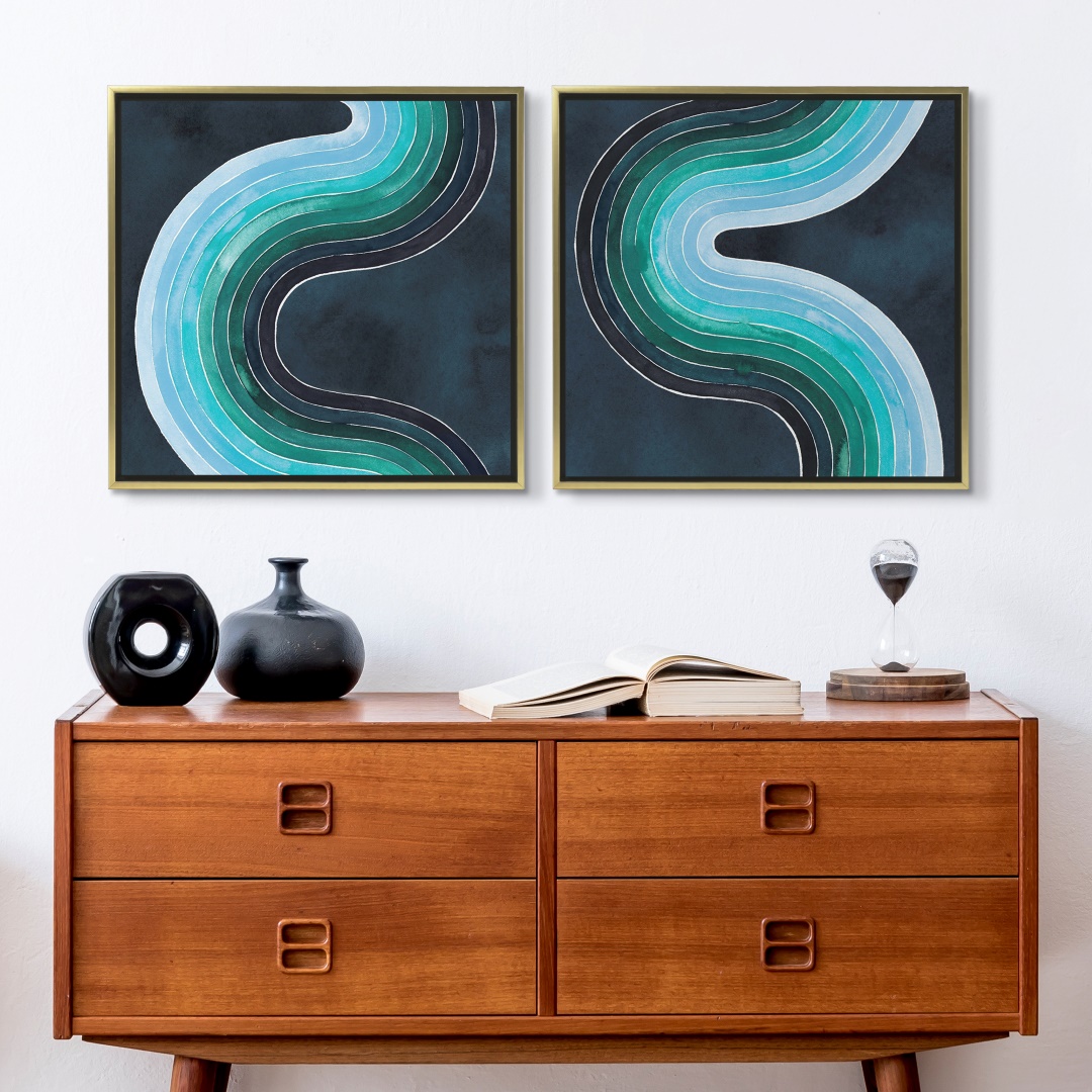 two blue swirling abstract canvas prints in a gold floating frame hung over a mid century table
