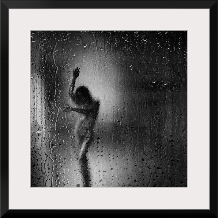 Square black and white fine art photograph of a nude woman through a rainy window glass.