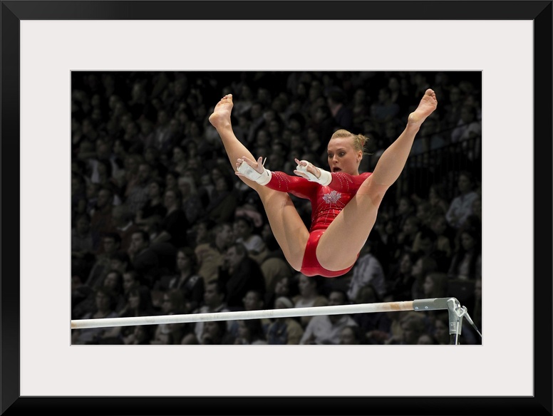 A female gymnast flies over the high bar with her legs raised up, arms outstretched ready to grab the bar.