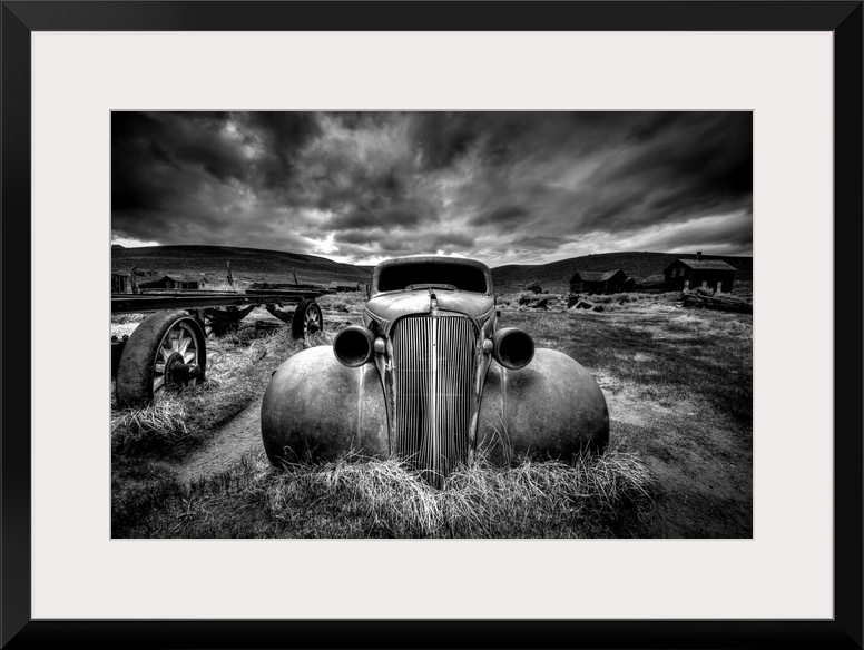 A black and white photograph of derelict vintage car sitting in a desert landscape.