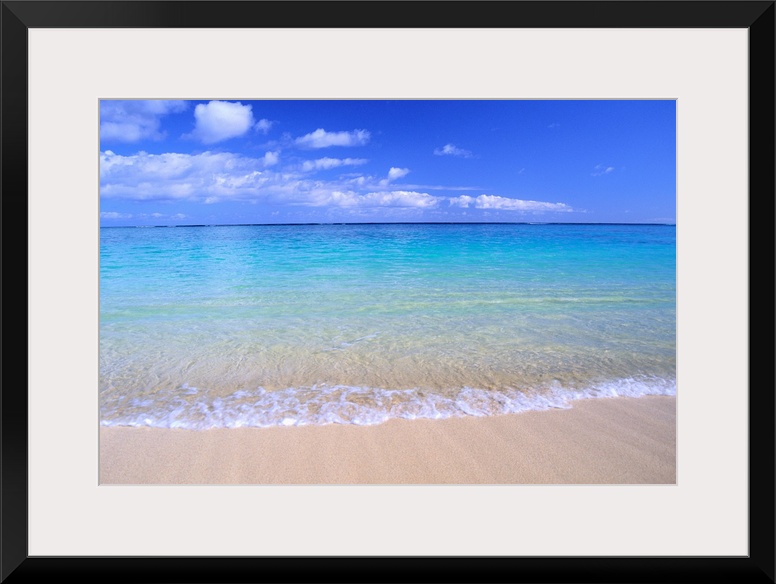 This home docor features a photograph that is a horizontal seascape of clean ocean water washing up on a sandy beach.