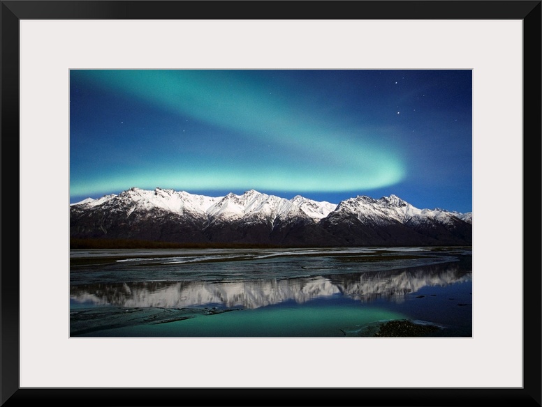 A landscape photograph of the aurora borealis and mountains reflecting in a lake filled with ice.