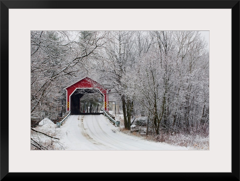 Snow covered trees surround a road that leads up to a covered bridge.