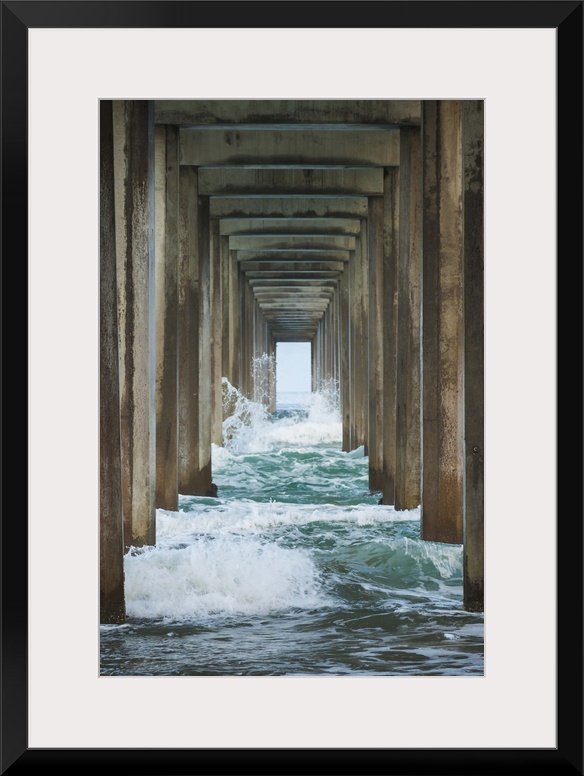 Photograph under a large pier looking out into the distance at the blue water.