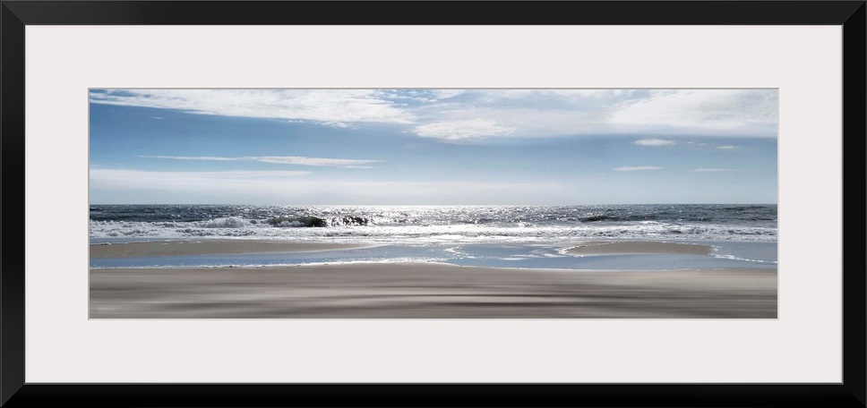 A panoramic photo illustrating a tranquil view of the beach as the sun shimmers on the sea.