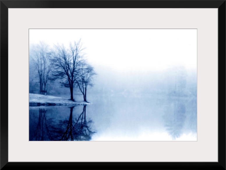 A photograph taken of a lake with bare trees off to the left side and more trees behind dense fog toward the back of the l...