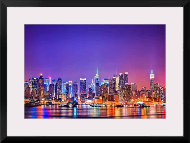 Photograph of New York skyline at night with the Hudson River in foreground.  The building lights are reflected in the water.