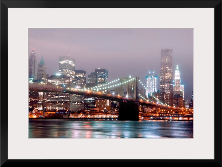 A misty night scene illuminated by urban lights of downtown Manhattan photographed from the Brooklyn shore.