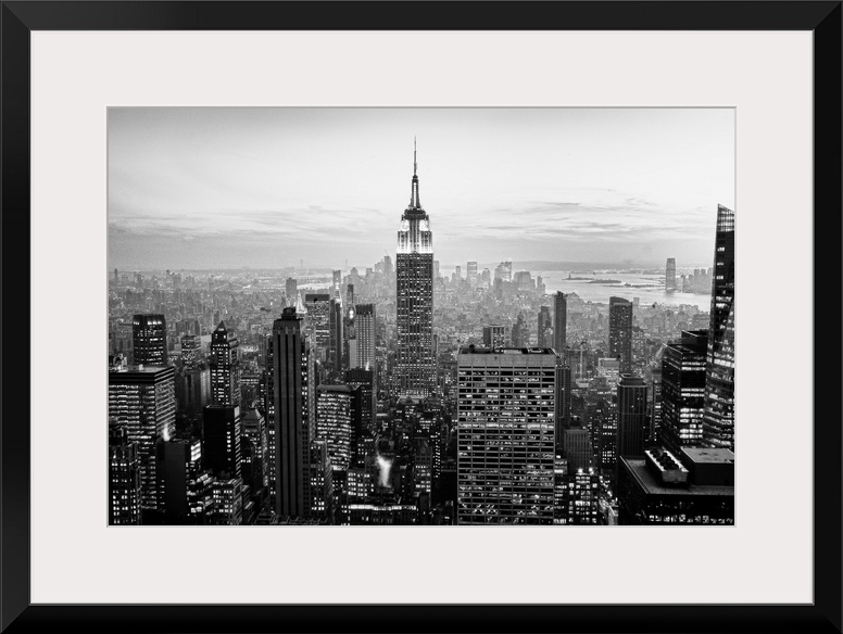 High angled photograph of city buildings at dusk.  The building windows are filled with light creating little rectangle pa...