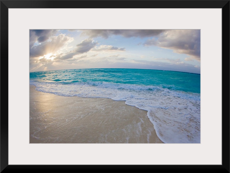 From the National Geographic Collection a wide angle photograph of the sun setting behind clouds while waves washed up aga...