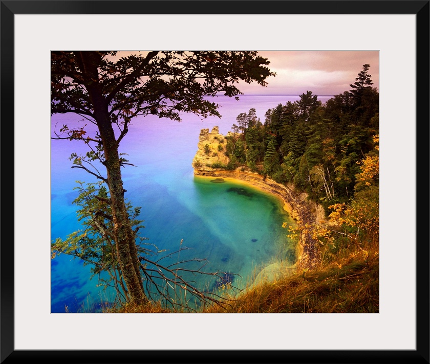An immense cliff is covered with various trees and thick foliage that curves and overlooks Lake Superior.