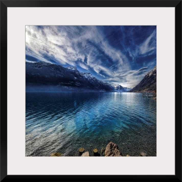 This square shaped decorative wall art is a landscape photograph of a lake surrounded by snow covered mountains beneath a ...