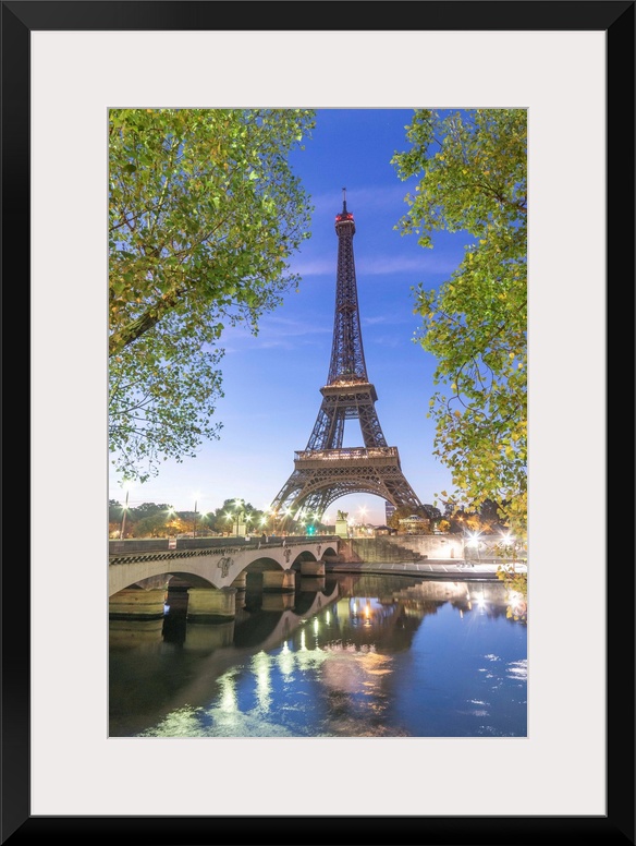 Early morning for the Eiffel tower in Paris, facing the Jena bridge with green trees around and lights.