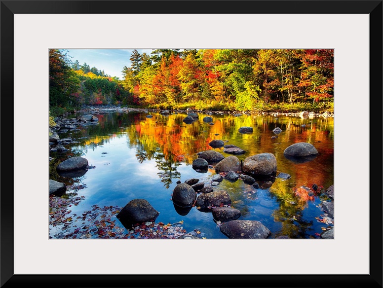 Fine art photo of bright colors of a forest in autumn being reflected in a pond full of rocks.