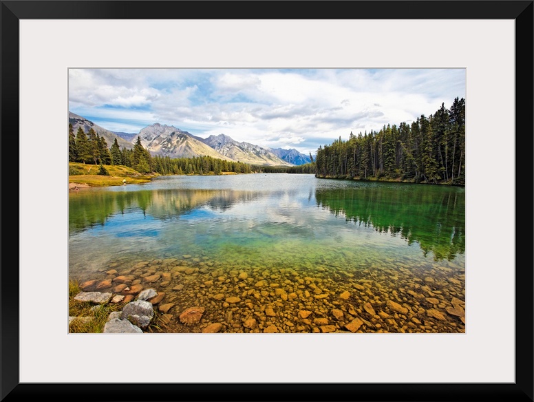 Giant photograph taken from the rocky shores of a lake that is surrounded by dense forests and snow covered mountains in t...