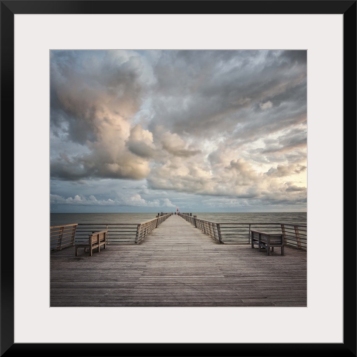 A wooden pier leading to the ocean with dramatic clouds above.