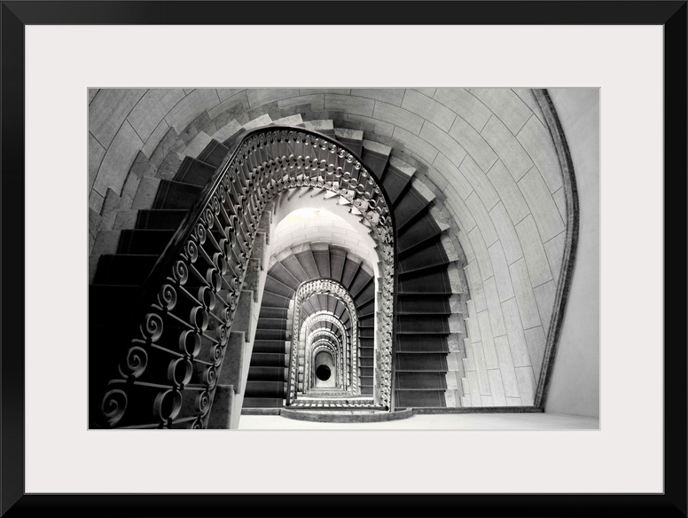 This architectural photograph looks down a historic stairwell lined with tile and iron work banister.
