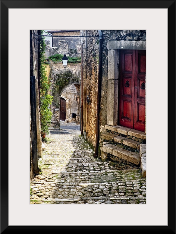 Cobblestone street in Sermoneta, Italy, with a red door on the side.