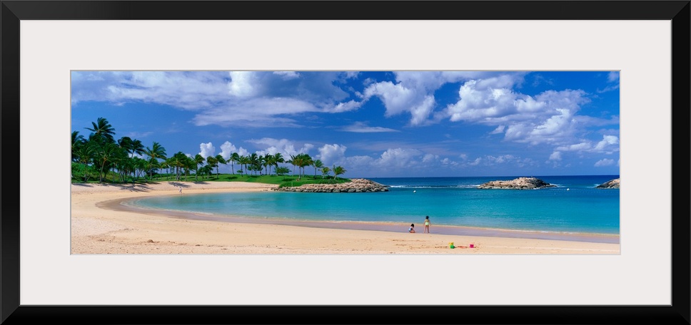 A panoramic photograph of a tropical cover on an island lined with palm trees and clear water.