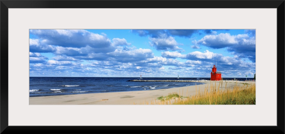 Panoramic photograph of a large lighthouse next to a dock on a sandy beach in Holland, Michigan during a sunny day.  The w...